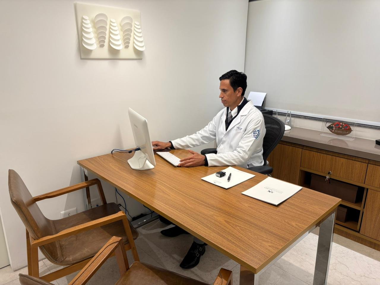 urologista-particular Urologista particular Dr. Marco Nunes em seu consultório, usando jaleco branco e trabalhando no computador, transmitindo profissionalismo e dedicação no atendimento.
