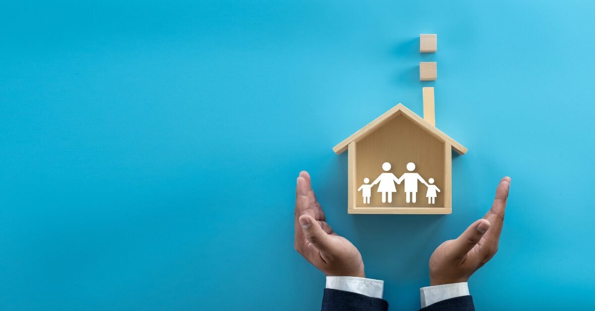 Mãos protegendo uma casa de madeira com símbolo de família, representando segurança, saúde e bem-estar no lar