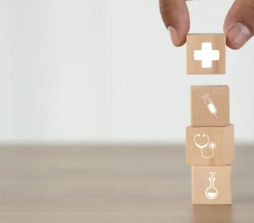 Blocos de madeira com ícones de saúde sendo empilhados, simbolizando cuidados preventivos e impacto do ambiente na longevidade.