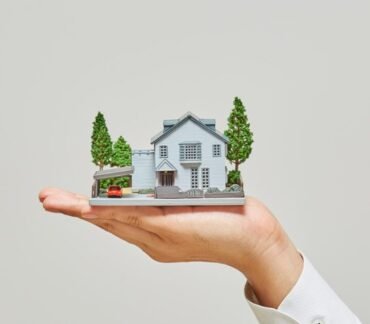 Casa em miniatura apoiada na mão, representando como o endereço e o estilo de vida influenciam a saúde, o bem-estar e a longevidade.