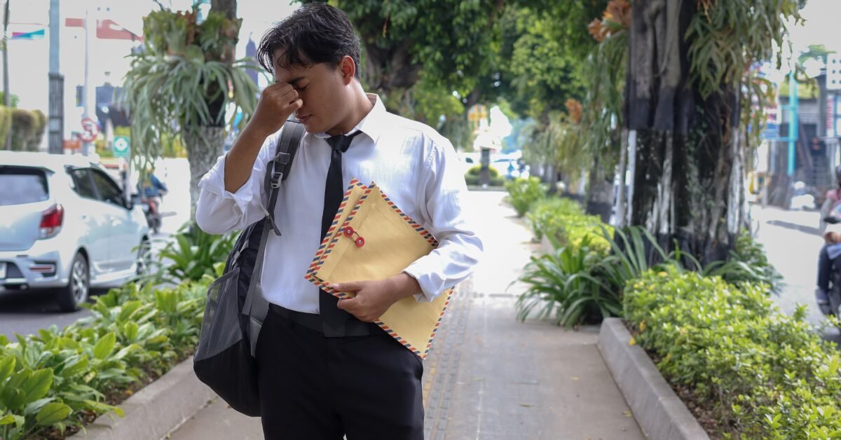 Homem de camisa social e gravata, com expressão de cansaço, segurando o rosto na calçada.