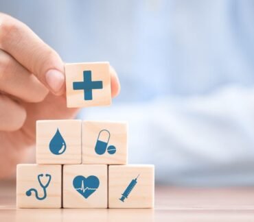 Blocos de madeira com ícones de saúde empilhados, representando como qualidade de vida, prevenção e ambiente impactam a longevidade.