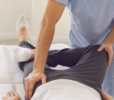 Profissional de saúde realizando alongamento da perna e do quadril de um homem deitado em maca.